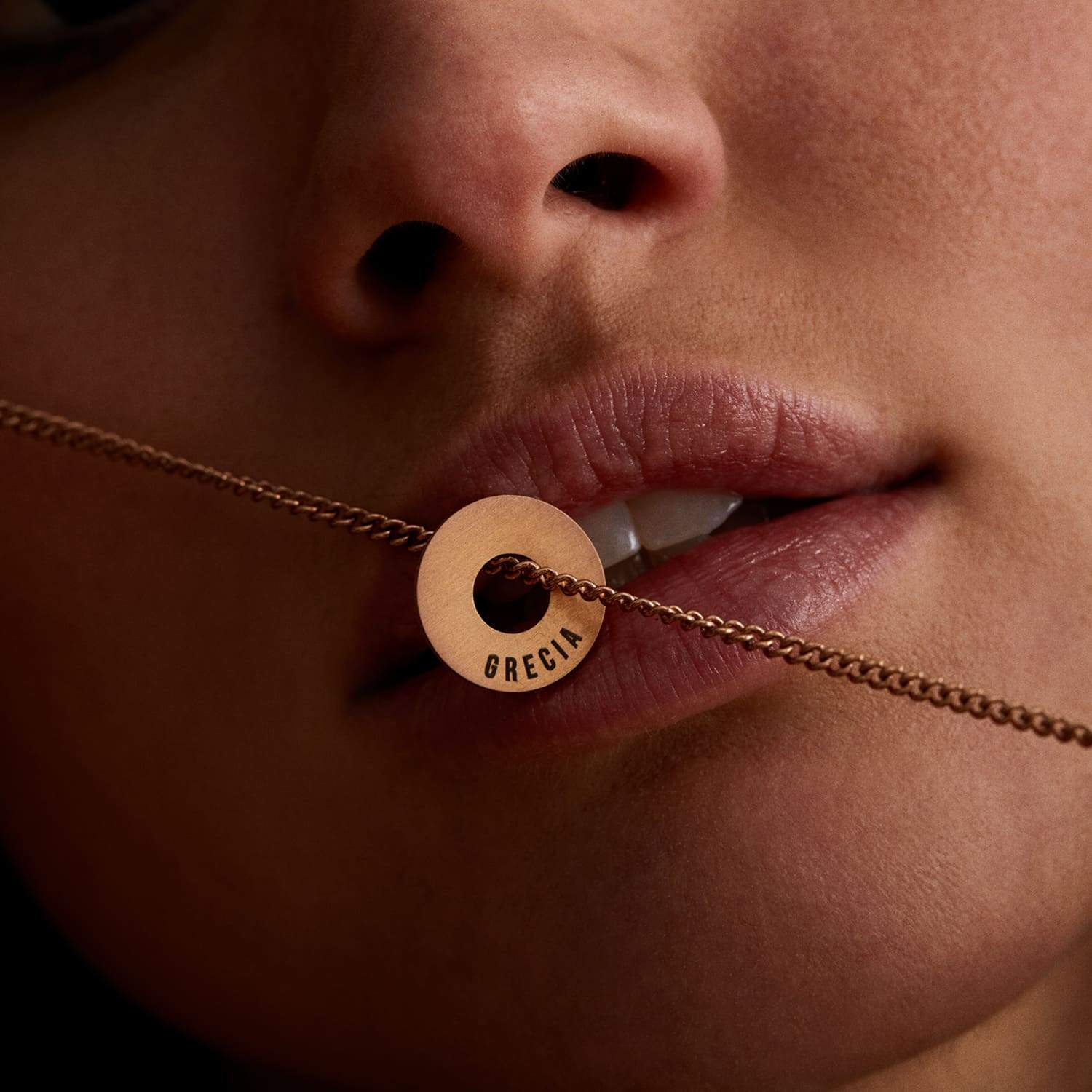 Anilla® en oro rosa con ORGULLO grabado sostenida entre los labios