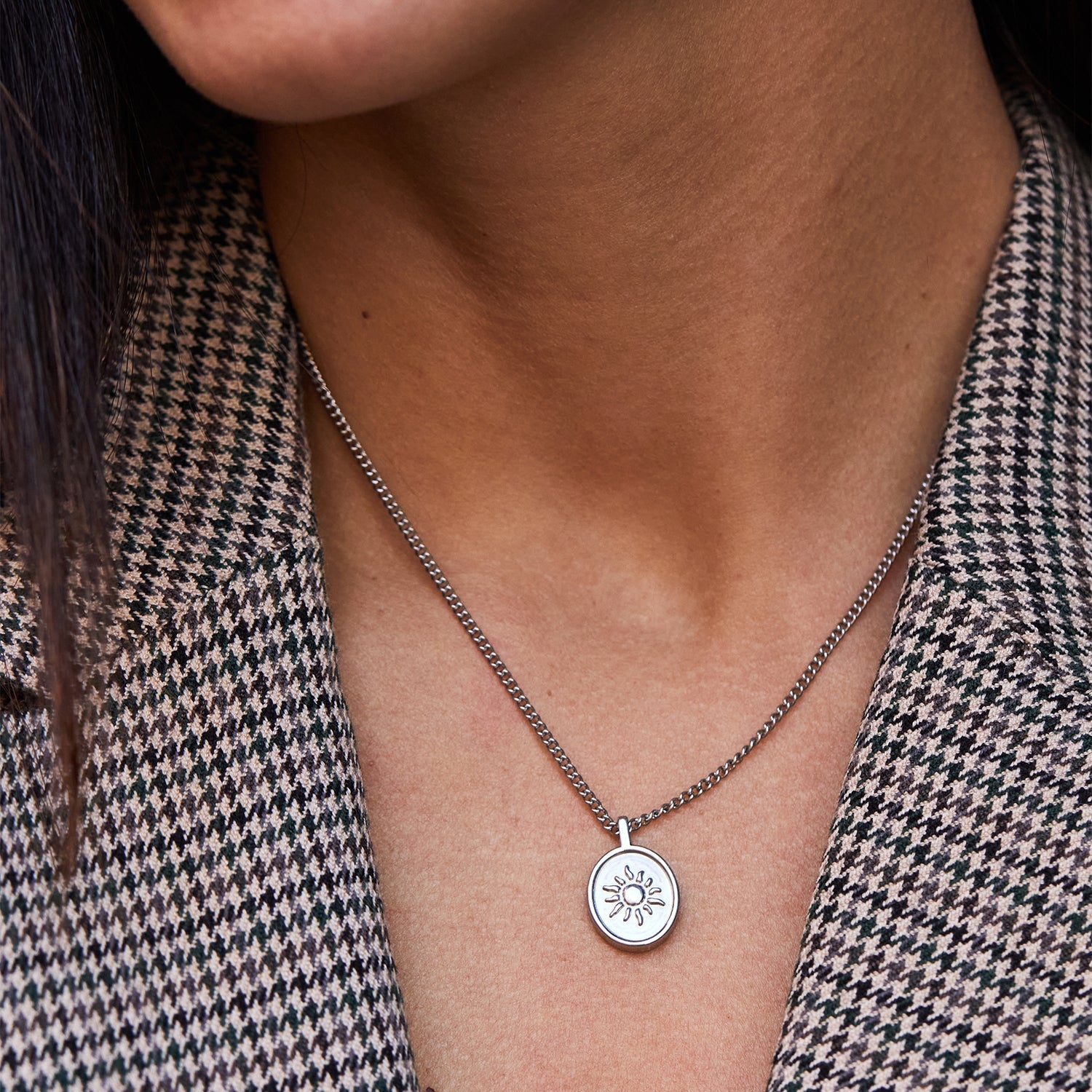 Collar Sentinel® en acero con medalla de sol llevado con chaqueta de pata de gallo