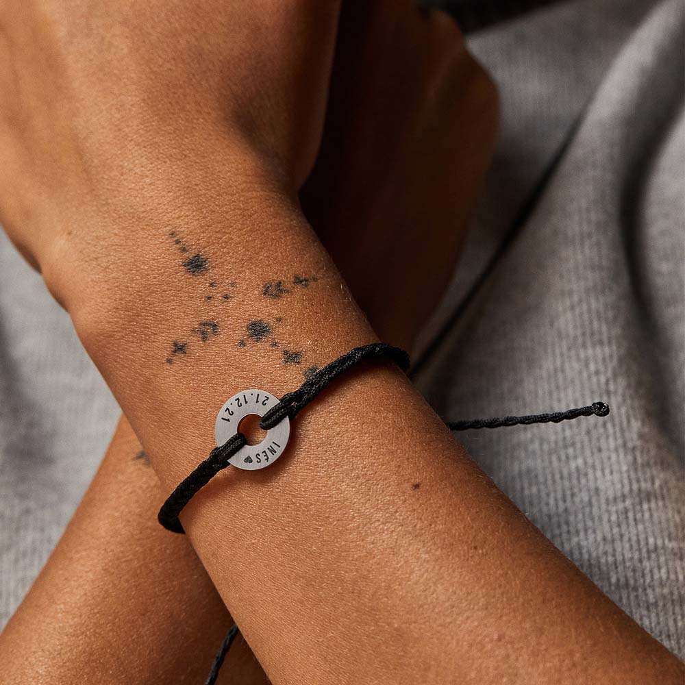 Pulsera MyWord® negra con anilla en acero en la muñeca, sobre prenda gris