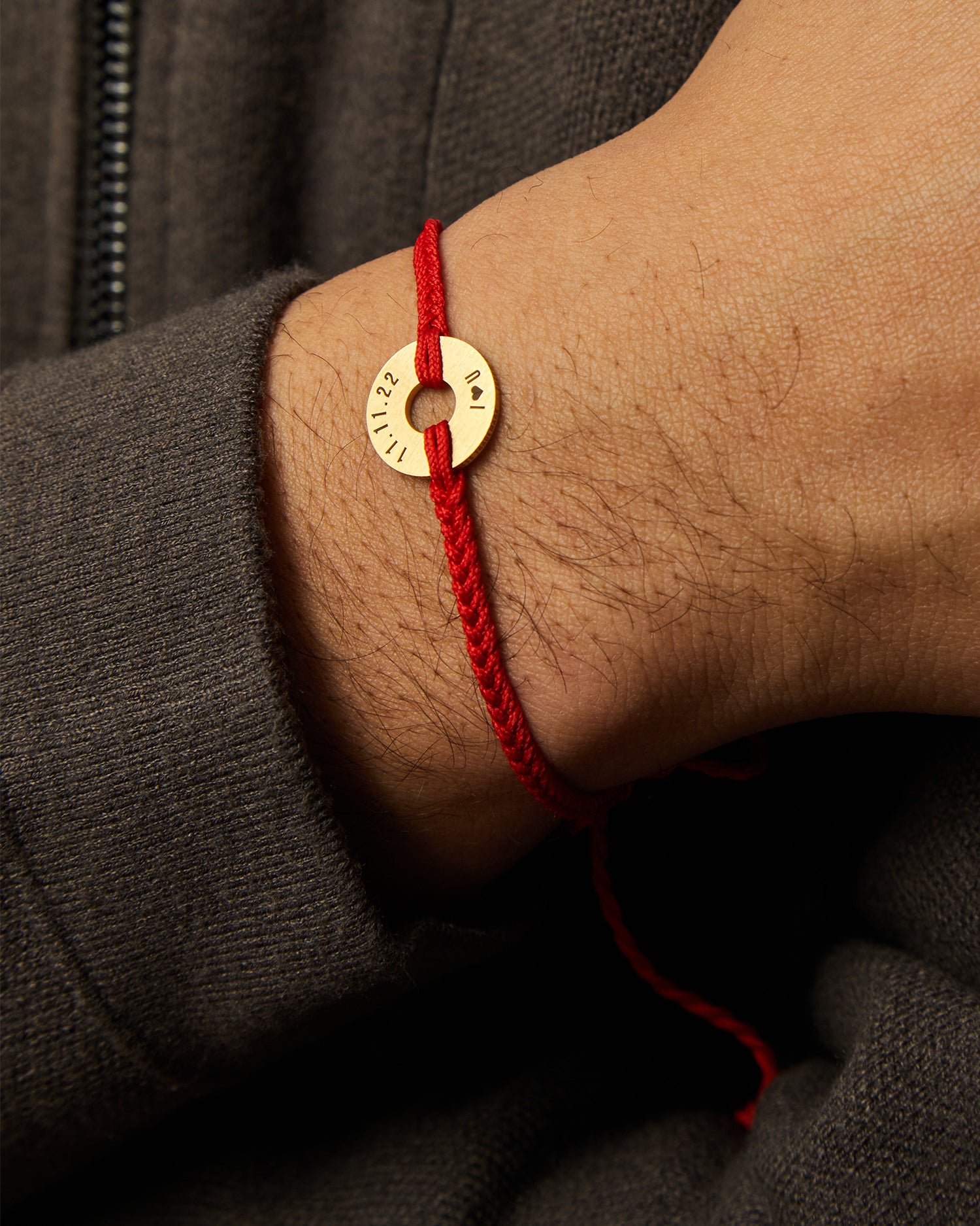 Pulsera MyWord® roja con anilla dorada grabada en la muñeca, sobre prenda oscura
