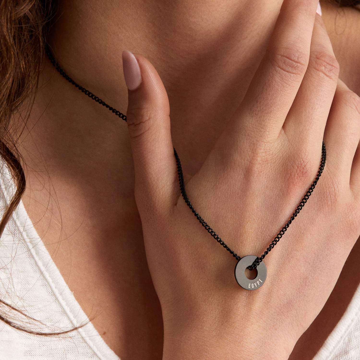 Anilla® negra y cadena Botany sobre camiseta blanca, con la mano al cuello