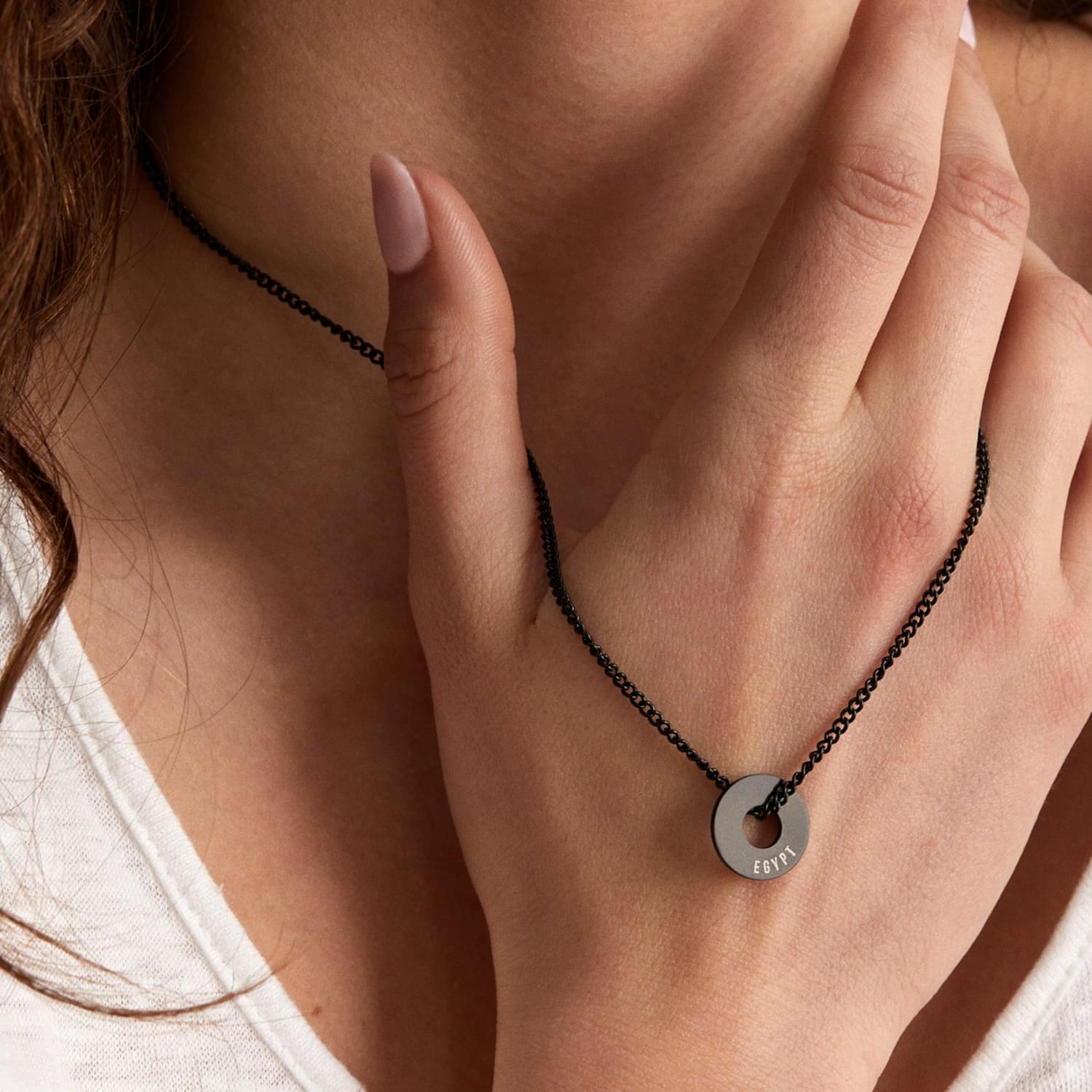 Anilla® negra en cadena fina llevada al cuello con la mano cerca
