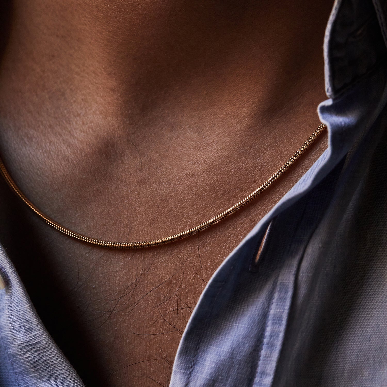 Collar Boa® dorado de eslabón tipo serpiente sobre el cuello, con camisa abierta