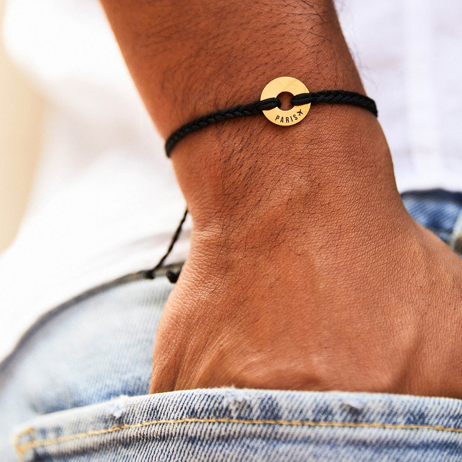 Pulsera MyWord® de cordón negro y anilla dorada sobre la muñeca, junto a un vaquero