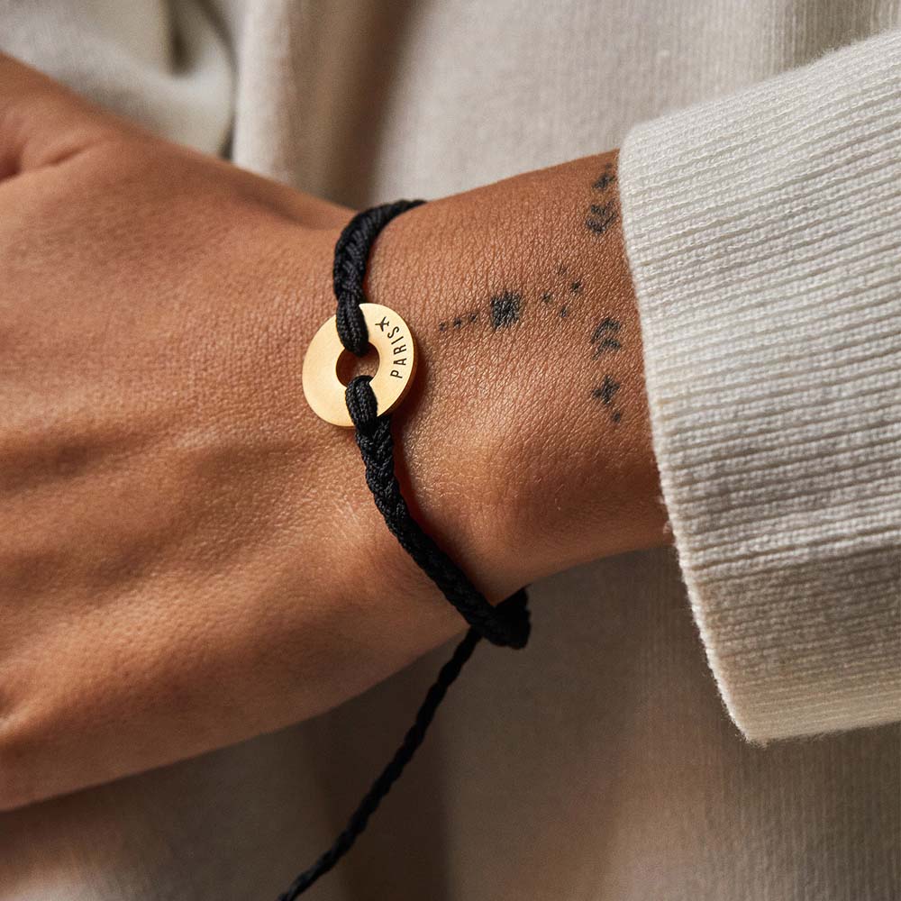 Pulsera MyWord® negra con anilla dorada grabada en la muñeca