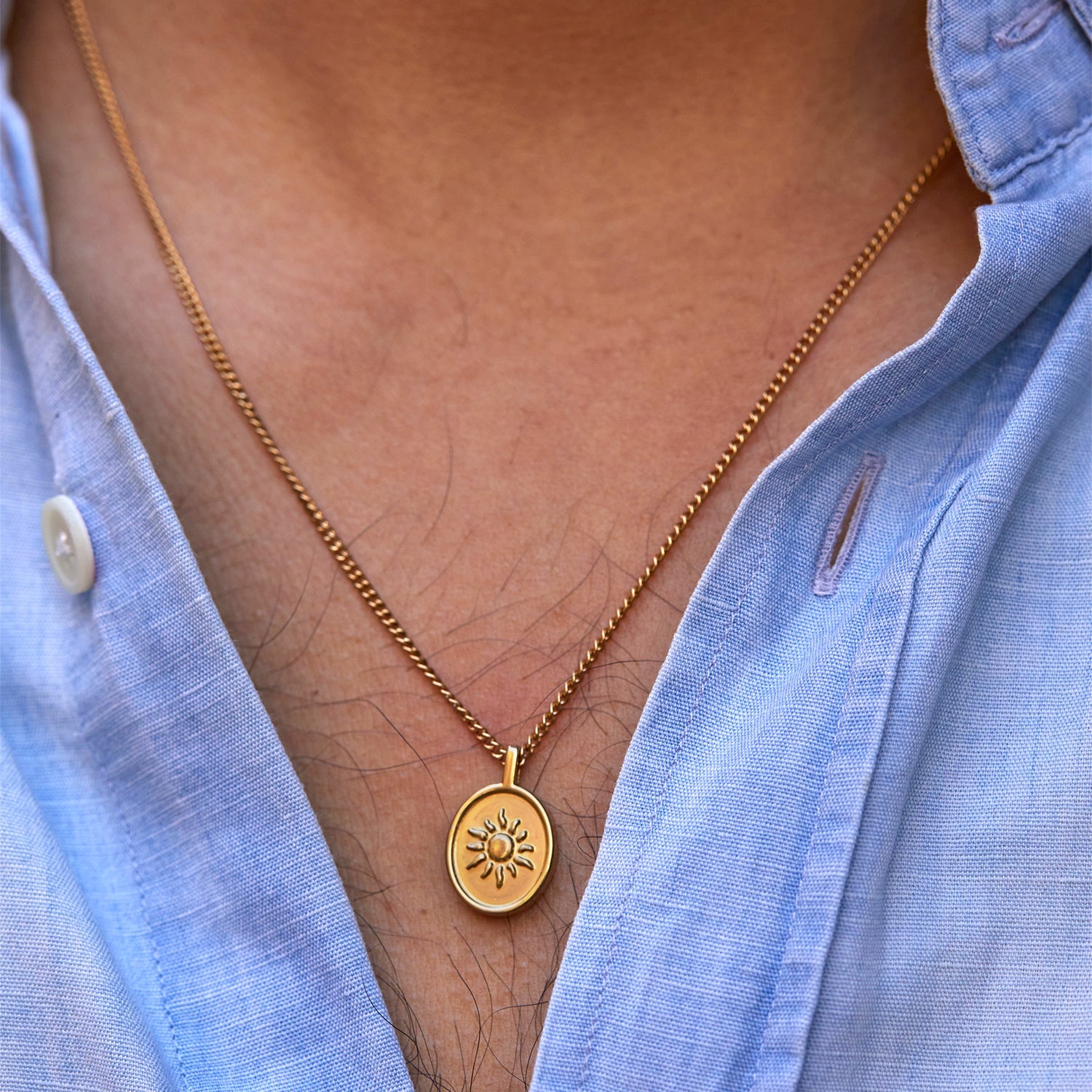 Medalla Sentinel® dorada con relieve de sol sobre una camisa azul abierta