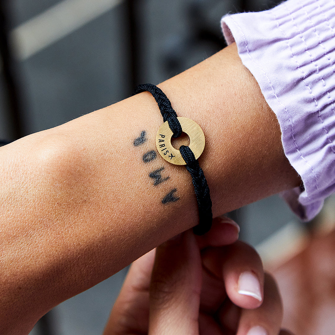 Pulsera MyWord® de cordón negro y anilla dorada puesta en la muñeca