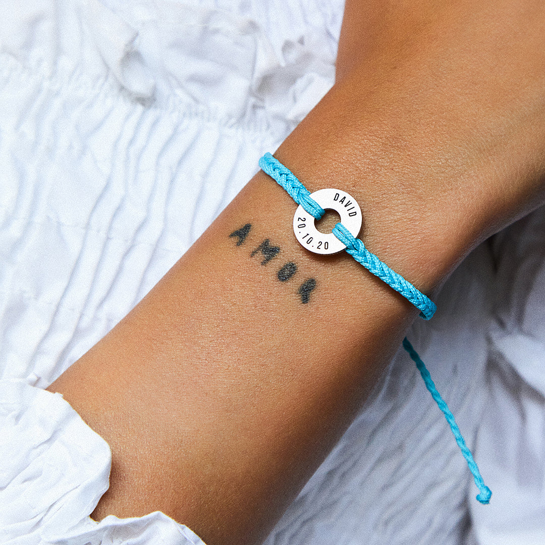 Pulsera MyWord® azul con anilla grabada en la muñeca, sobre prenda blanca