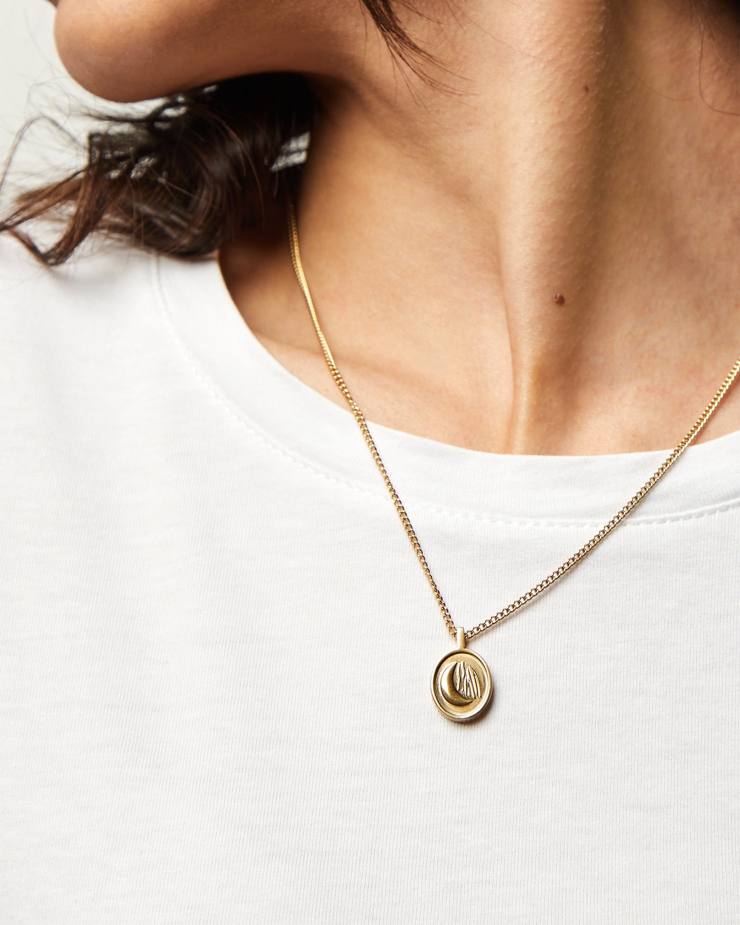 Collar Sentinel® dorado sobre una camiseta blanca, con la medalla centrada