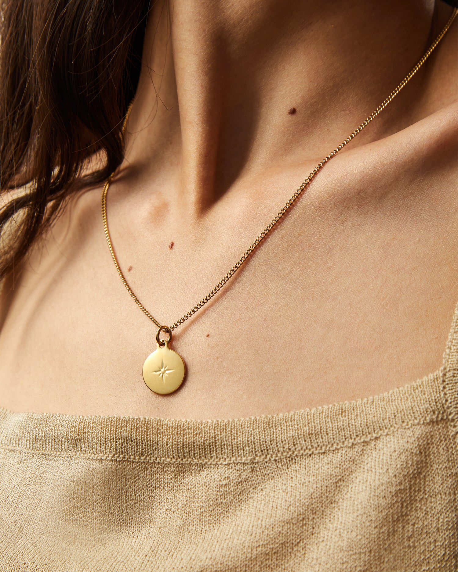 Collar Namib® dorado sobre un top beige, con el colgante centrado