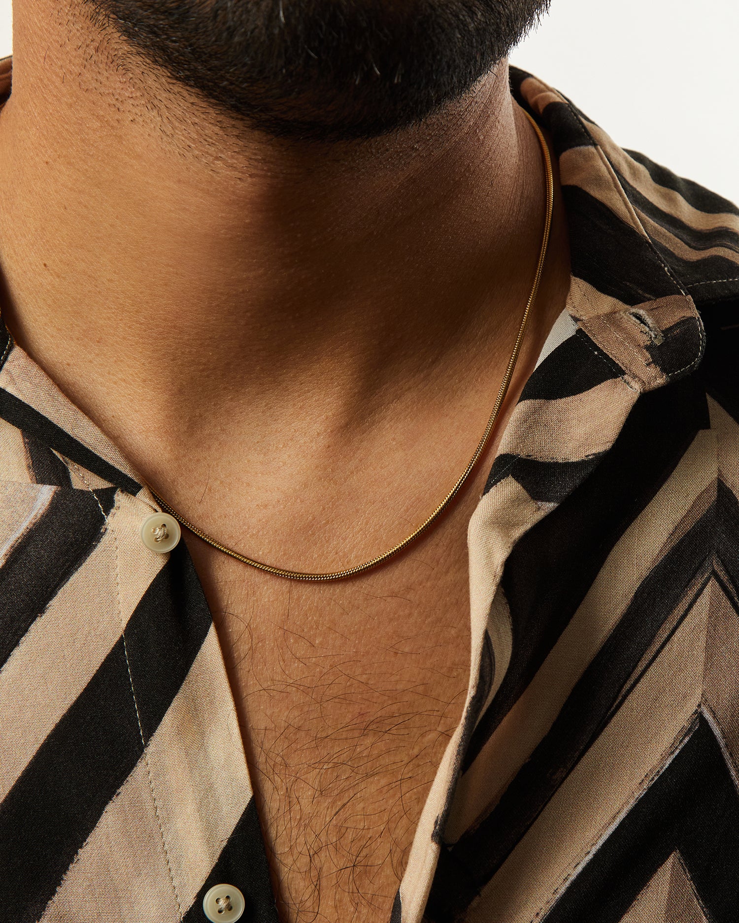 Collar Boa® dorado llevado con una camisa de rayas abierta