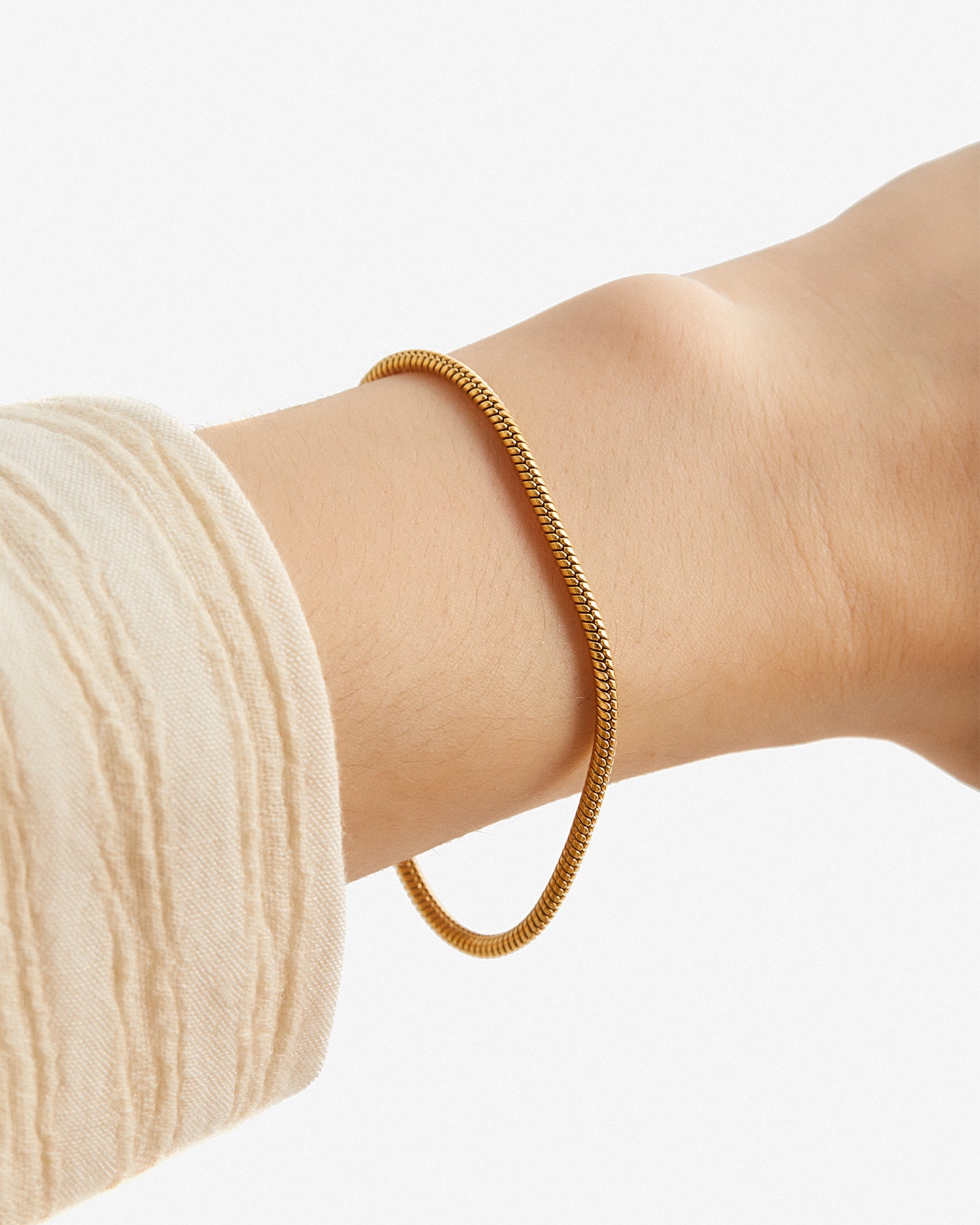 Pulsera Boa® dorada puesta en la muñeca junto a un puño de punto claro