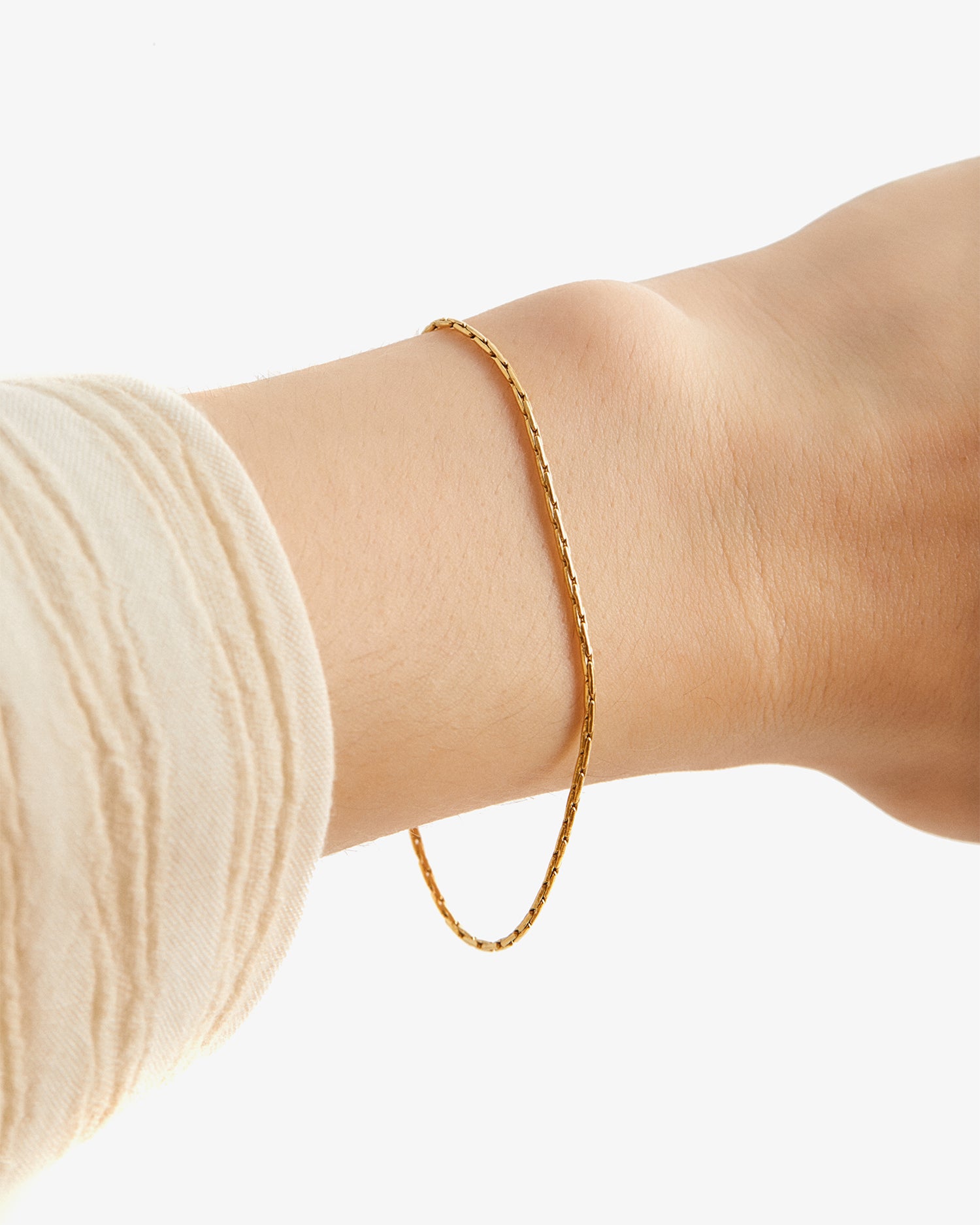 Pulsera Mamba® dorada en la muñeca junto a un puño de punto claro
