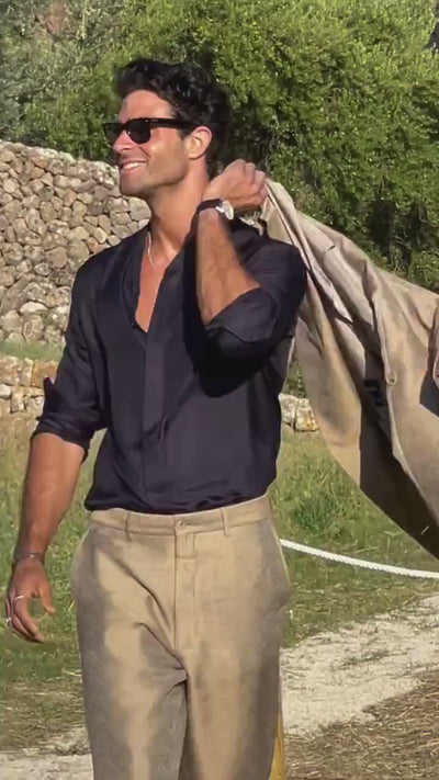 Hombre con con colgante circle personalizable y estilo mediterráneo bailando junto a un muro de piedra, chaqueta al hombro